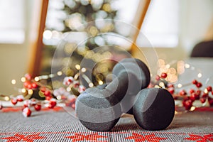 Healthy lifestyle during Christmas feasting period concept. Black dumbbells with Christmas ornaments.