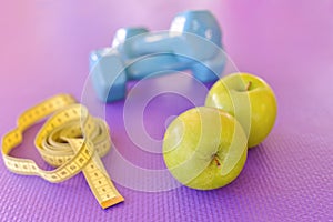 Healthy lifestyle concept - green apple with dumbbells and yellow measuring tape