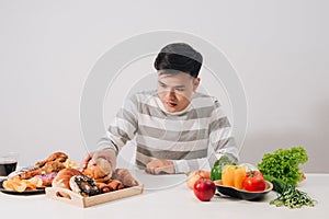 Healthy lifestyle concept - smiling young man comparing healthy and unhealthy food. fresh vegetables and hamburger