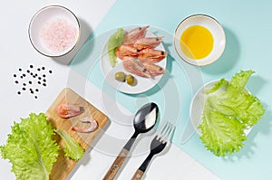 Healthy lifestyle - cooking of fresh salad of prawn, green salad, olive, black pepper, pink salt in sunlight with shadow, flat lay