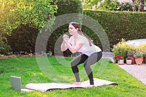 Healthy lifestyle. Exercising at home. Doing fitness online. Beautiful young woman doing sport in garden outdoors