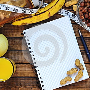 Healthy lifestyle; fitness bottle; fruits oranges; apples and bananas; hazelnuts and peanuts; orange juice, a pen and a notebook a