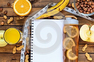 Healthy lifestyle; fitness bottle; fruits oranges; apples and bananas; hazelnuts and peanuts; orange juice, a pen and a notebook