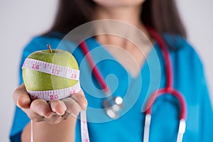 Healthy lifestyle, food and sport concept. Close up Smiling doctor woman hand holding measuring tape around fresh green apple