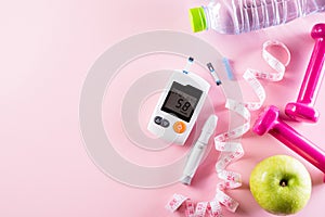 Healthy lifestyle, food and sport concept. Top view of diabetes tester set with athlete`s equipment measuring tape pink dumbbell,