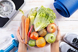 Healthy lifestyle, food and sport concept. Top view of woman hand holding plate of fresh vegetables and fruits with athlete`s