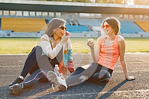 Healthy lifestyle and healthy food concept. Smiling fitness mother and teen daughter together eating apple sitting on stadium