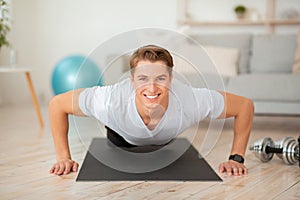 Healthy lifestyle at home during quarantine. Smiling handsome muscular guy doing push-ups