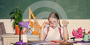 Healthy lifestyle. Kid student in school. Schoolgirl sit desk chalkboard background. Girl small child eating apple snack