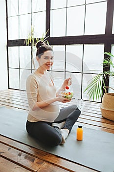 Healthy lifestyle and nutrition during pregnancy. Young pregnant woman eating salad on yoga mat