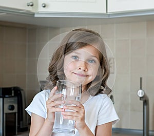 Healthy lifestyle. Portrait of happy smiling young girl with glass. Child drinking fresh water in the kitchen at home. Healthcare