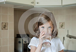 Healthy lifestyle. Portrait of happy smiling young girl with glass. Child drinking fresh water in the kitchen at home. Healthcare