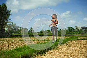 Healthy lifestyle portrait of young happy and fit Southeast Asian Thai runner woman in running workout outdoors at green field bac