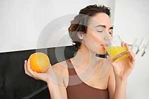 Healthy lifestyle and sport. Beautiful smiling woman, drinking fresh orange juice and holding fruit in her hand