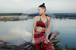 Healthy lifestyle and sport concepts. Woman in fashionable sportswear rests after a sports active training near the lake. Listens