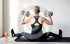 Rear view of young blond woman working out with dumbbells showing her back and arms muscles