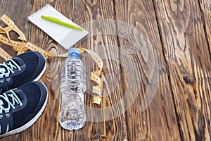 Healthy lifestyle and sports background. Sports shoes, Notepad and pen, and water bottle on wooden background with copyspace,
