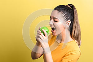 Healthy lifestyle. starving girl on diet about to bite an apple with against yellow background