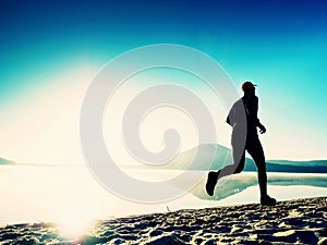 Healthy lifestyle. Tall young man runner is running on sunrise seaside. Man jump in sand