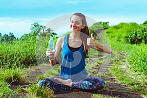 Healthy lifestyle. Woman with bottle of water in lotus pose. Thumb up