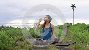 Healthy lifestyle. Woman drink water in lotus pose on natute background.