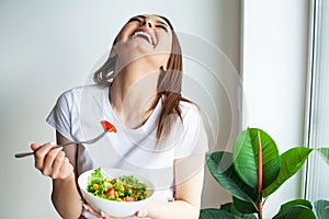 Healthy lifestyle woman eating salad smiling happy in light kitchen