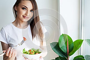 Healthy lifestyle woman eating salad smiling happy in light kitchen