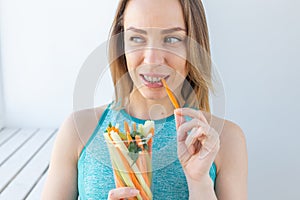 Healthy lifestyle woman eating vegetables smiling happy indoors. Young female eating healthy food close-up.