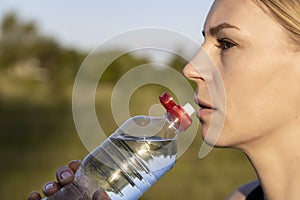 Healthy Lifestyle. Woman of European appearance outdoors drinks water from a bottle, close up.