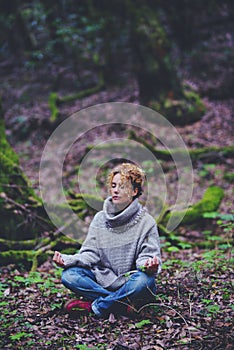 Healthy lifestyle woman sitting on the ground in lotus yoga position with green forest nature woods around. Female people and zen