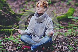 Healthy lifestyle woman sitting on the ground in lotus yoga position with green forest nature woods around. Female people and zen