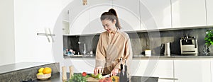 Healthy lifestyle. Young woman in bathrobe preparing food, chopping vegetables, cooking dinner on kitchen counter