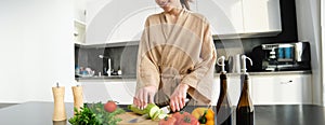 Healthy lifestyle. Young woman in bathrobe preparing food, chopping vegetables, cooking dinner on kitchen counter