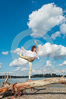 Healthy lifestyle young woman practice yoga on  dried trunk on the river beach fresh air sunny summer day