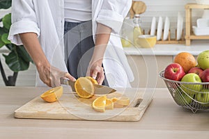 Healthy living and Vegan food. Cooking vegan food. A young woman is cutting an orange on a wooden cutting board