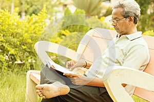 Healthy looking senior man in late 70s sitting in garden at home and reading book, outdoor - old man relaxing at Park by seriously