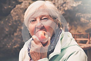 Healthy looking senior woman with grey hair eating apple outside