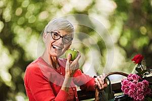 Senior woman with grey hair holding apple outside in the park