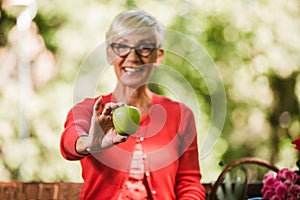 Senior woman with grey hair holding apple outside in the park