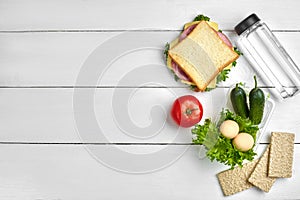 Healthy lunch box with sandwich, eggs and fresh vegetables, bottle of water on rustic wooden background. Top view with