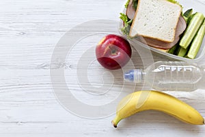 Healthy lunch box with sandwich, fruits and bottle of water on white wooden table, top view. From above, flat, overhead