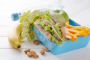 Healthy lunch box with sandwich, fruits, vegetables and bottle of water on white wooden table.