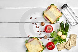 Healthy lunch box with sandwiches, eggs and fresh vegetables, bottle of water and nuts on rustic wooden background. Top