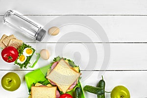 Healthy lunch box with sandwiches, eggs and fresh vegetables, bottle of water on rustic wooden background. Top view with