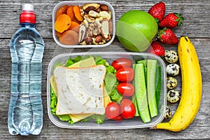 Healthy lunch boxes with sandwich, eggs and fresh vegetables, bottle of water, nuts and fruits