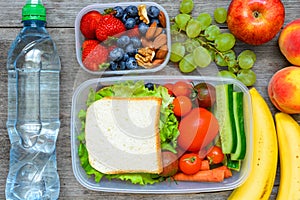 Healthy lunch boxes with sandwich and fresh vegetables, bottle of water, nuts and fruits