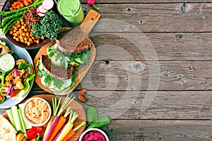 Healthy lunch food side border with nutritious hearty bowl, sandwiches, lettuce wraps and vegetables, top view over a wood backgro