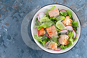 Healthy lunch salad with baked salmon fish, fresh radish, lettuce and lime. Top view