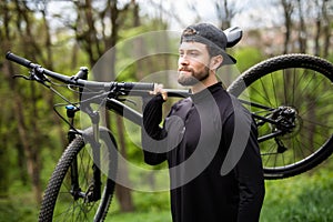 Healthy man bicycler carrying mountain bike while exploring in woods