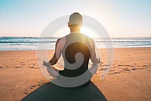 Healthy man practicing yoga and meditates on the beach at sunset or sunrise